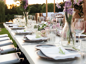 Romantisch gedekte dinertafel voor een bruiloft bij Dekker Zoetermeer, versierd met roze bloemen, elegant servies en wijnglazen aan het water in het warme avondlicht.
