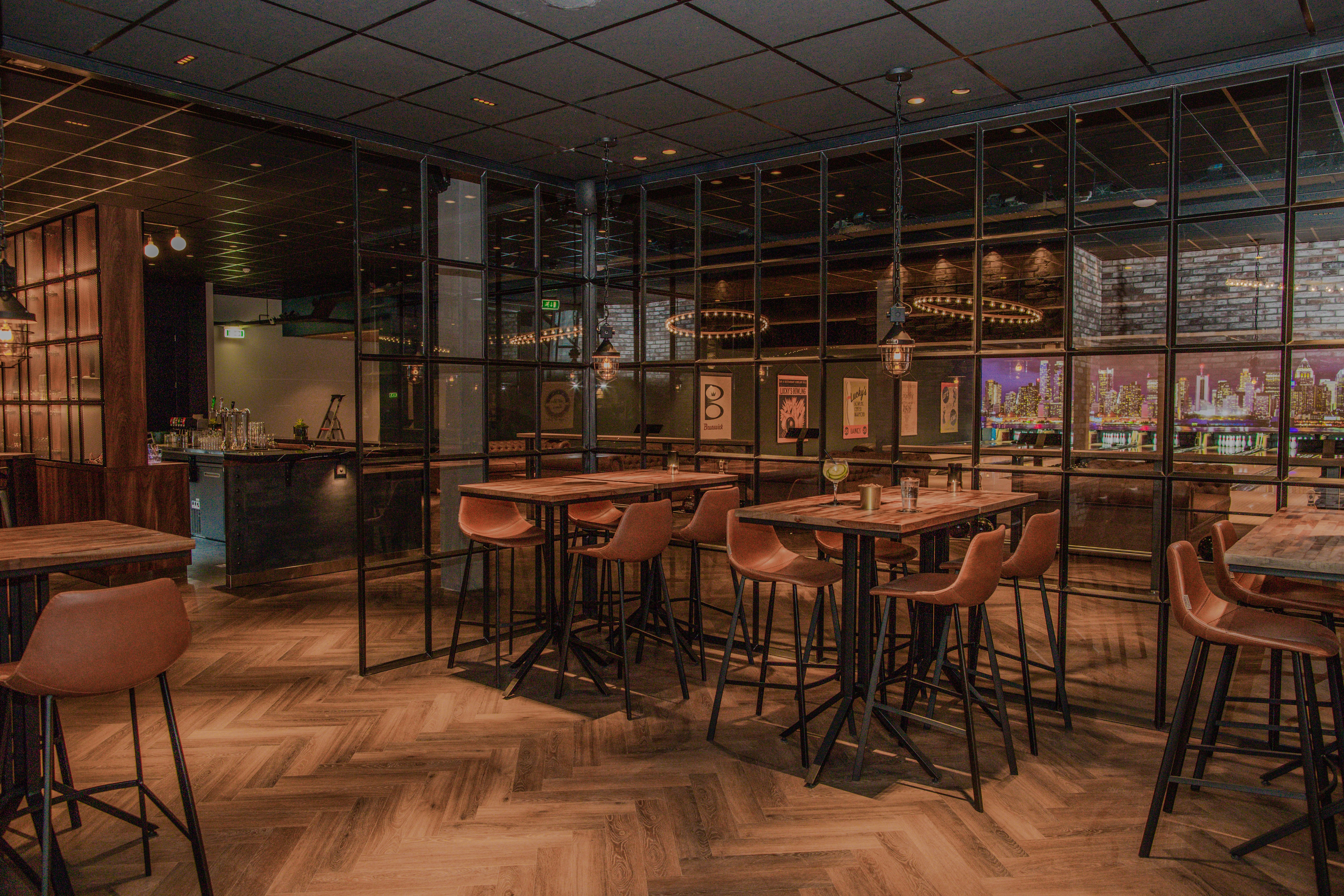 Sfeervolle bar en lounge bij Lucky's Bowling in Dekker Zoetermeer, met hoge houten tafels, comfortabele barkrukken en uitzicht op de bowlingbanen.