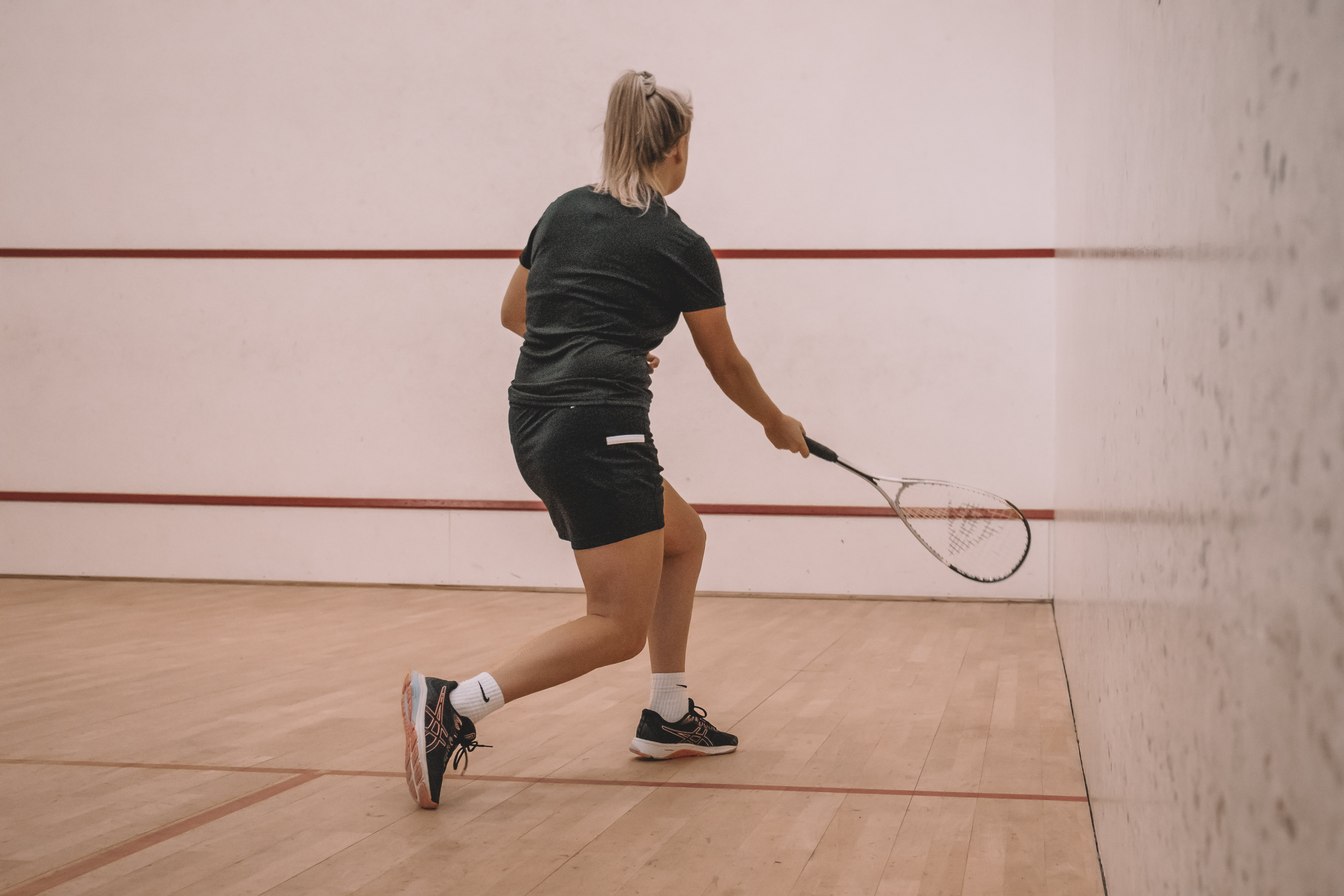 Sportieve vrouw speelt squash op een indoor squashbaan bij Dekker Zoetermeer en slaat met haar racket richting de muur.
