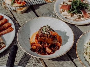 Een tafel vol heerlijke Italiaanse gerechten bij Sweet Lake Italy in Dekker Zoetermeer, met versgebakken pizza's, bruschetta, een smaakvol vleesgerecht en een glas witte wijn.