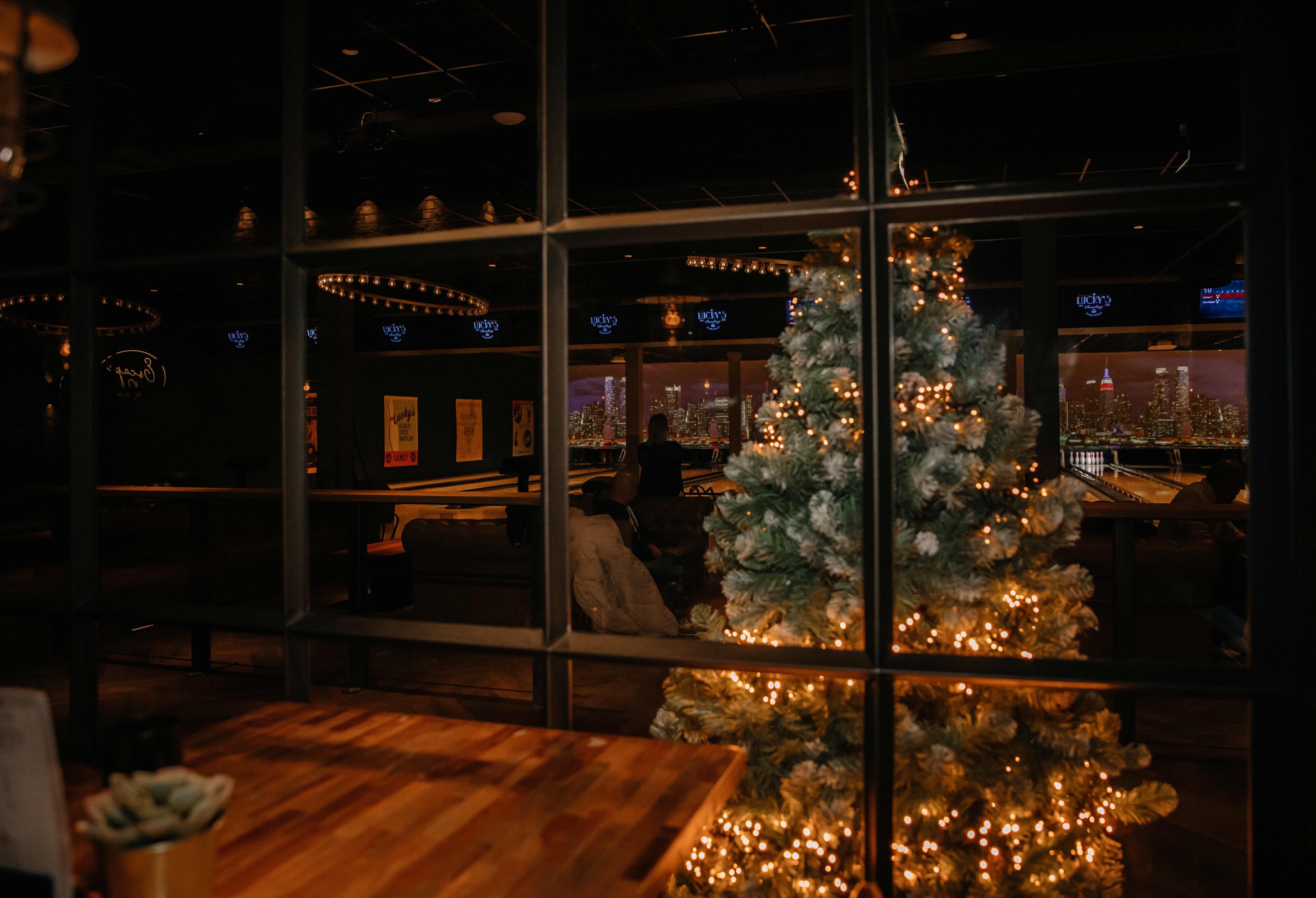 Sfeervolle kerstboom met warme lichtjes achter een glazen wand bij Lucky’s Bowling in Dekker Zoetermeer, met uitzicht op de verlichte bowlingbanen en gezellige zithoeken.