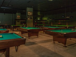Sfeervolle poolruimte bij Dekker Zoetermeer met meerdere pooltafels, groene biljartlakens en warme verlichting. Een gezellige locatie om samen te poolen met vrienden, familie of collega's.