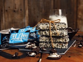 N'Joy Cookies & Cream proteïnerepen met witte chocolade en krokante stukjes, sfeervol gepresenteerd op een houten tafel.
