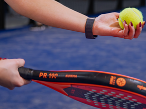 Close-up van een padelspeelster met een felgele padelbal en een rood-zwart padelracket op de blauwe padelbaan bij Dekker Zoetermeer.