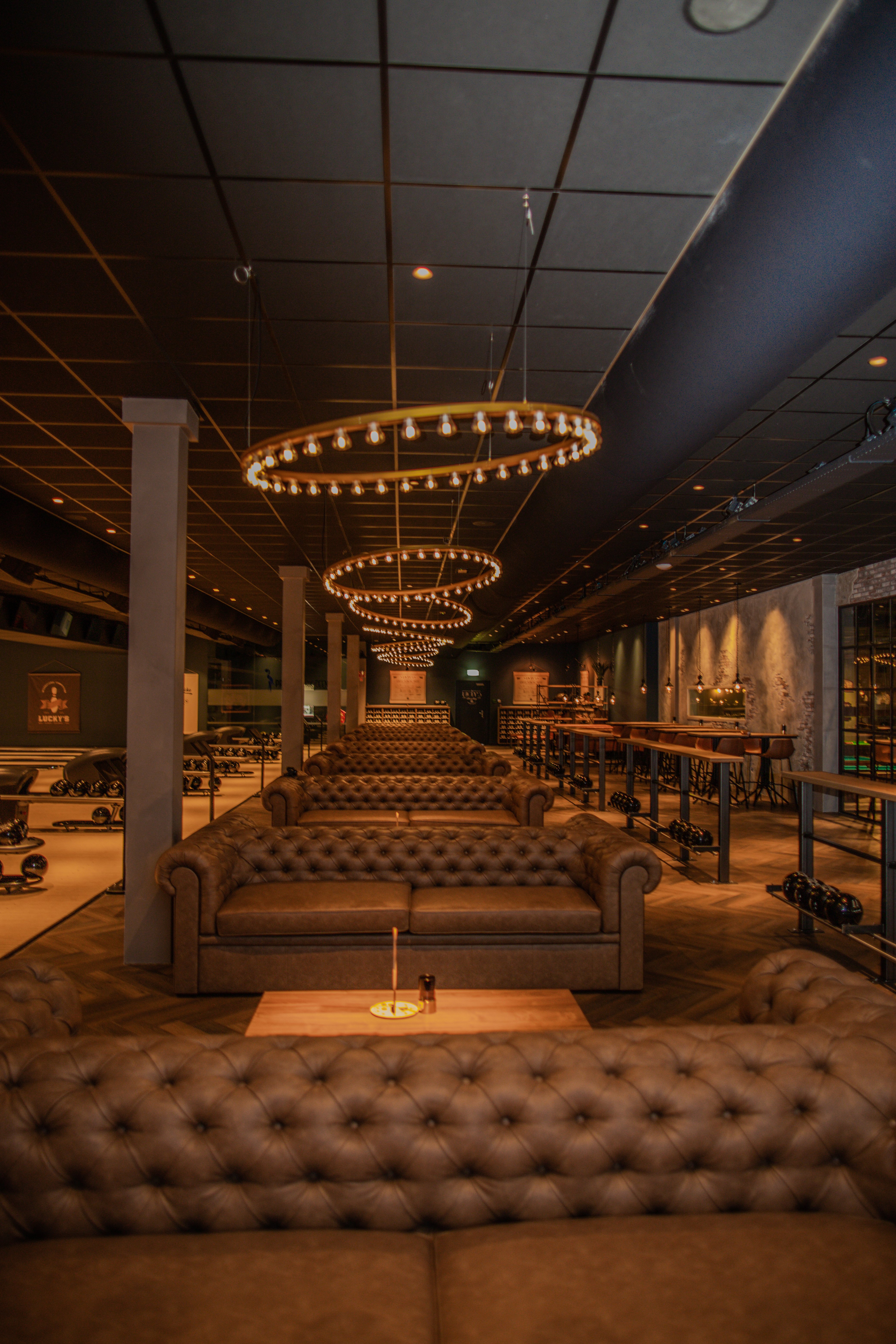 Sfeervol interieur van Lucky's Bowling bij Dekker Zoetermeer, met comfortabele Chesterfield banken, warme verlichting, bowlingbanen en een gezellige lounge.
