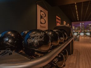 Bowlingballen met de tekst 'Tonight We Bowl' op de voorgrond, met sfeervol verlichte bowlingbanen bij Lucky's Bowling in Dekker Zoetermeer.