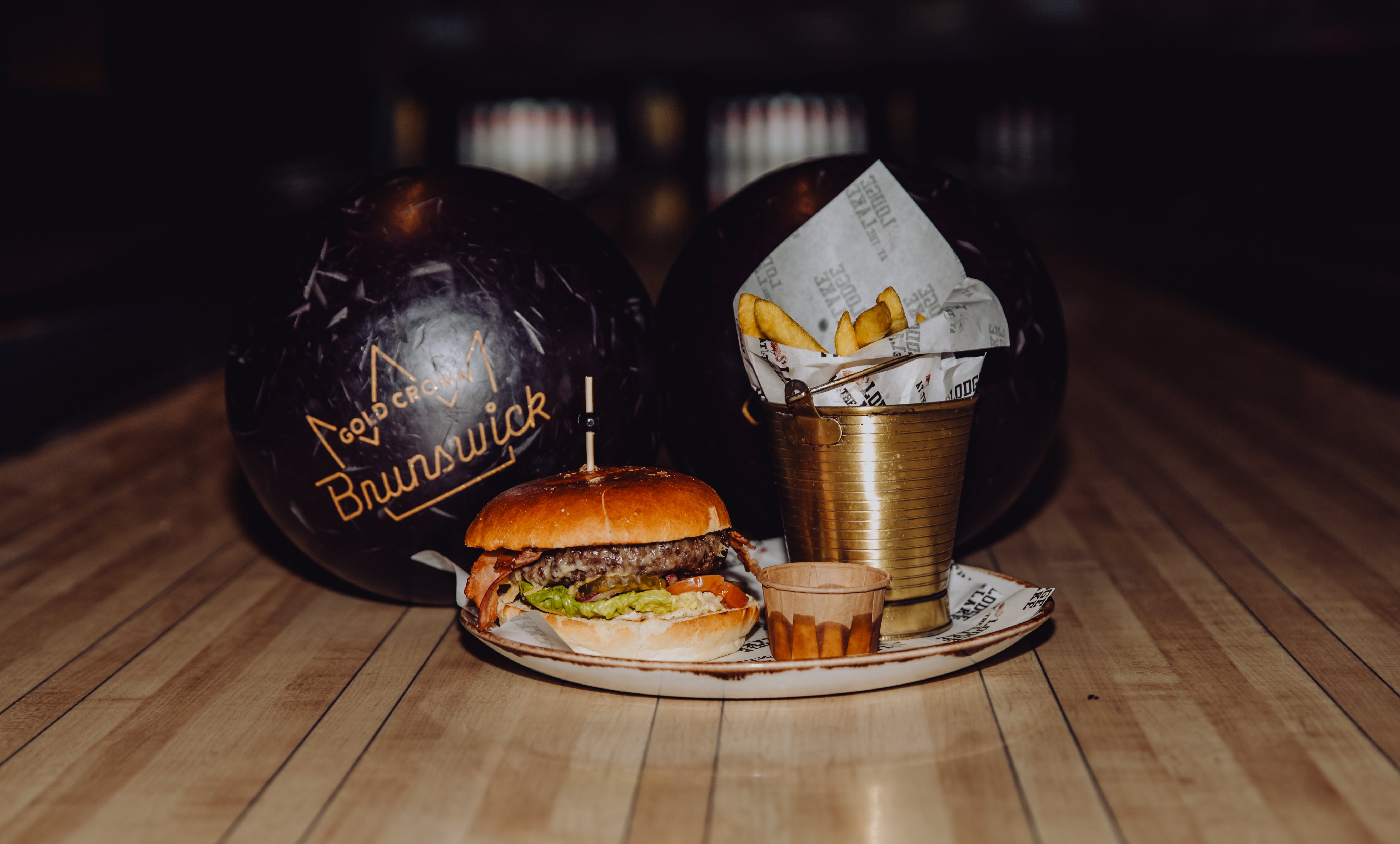Smakelijke hamburger met friet en saus, geserveerd voor twee bowlingballen bij Lucky’s Bowling in Dekker Zoetermeer. Een heerlijke combinatie van bowlen en gezellig eten.